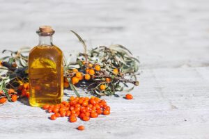 Glass jar filled with vibrant orange seabuckthorn oil alongside a fresh sea buckthorn branch with berries, set on a rustic wooden background, highlighting the natural purity of the oil